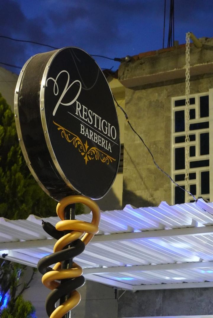 Letrero exterior de Prestigio Barberia, negro con dorado, al caer la noche.